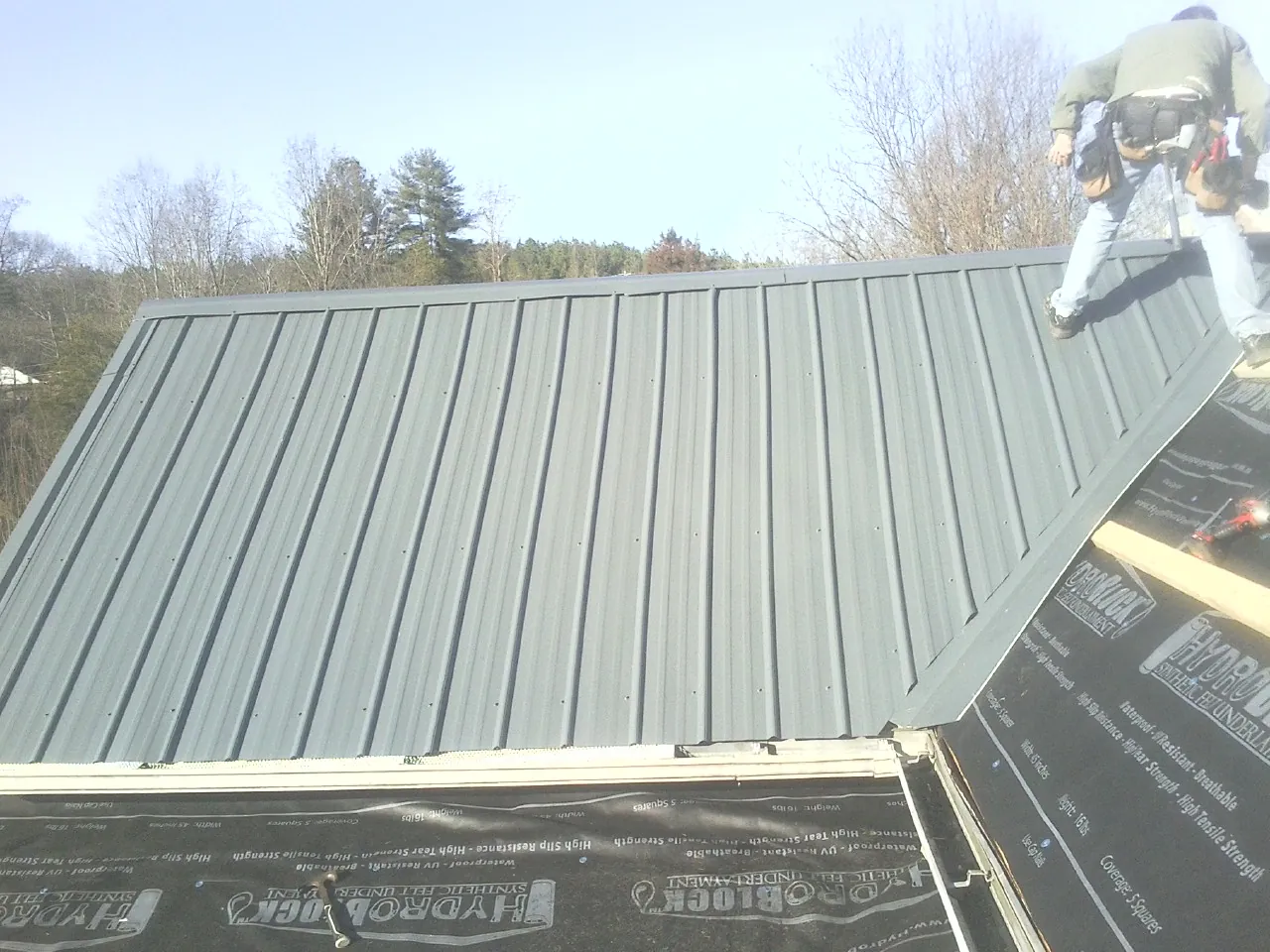Crew installing dark green standing seam panels over synthetic underlayment in Converse