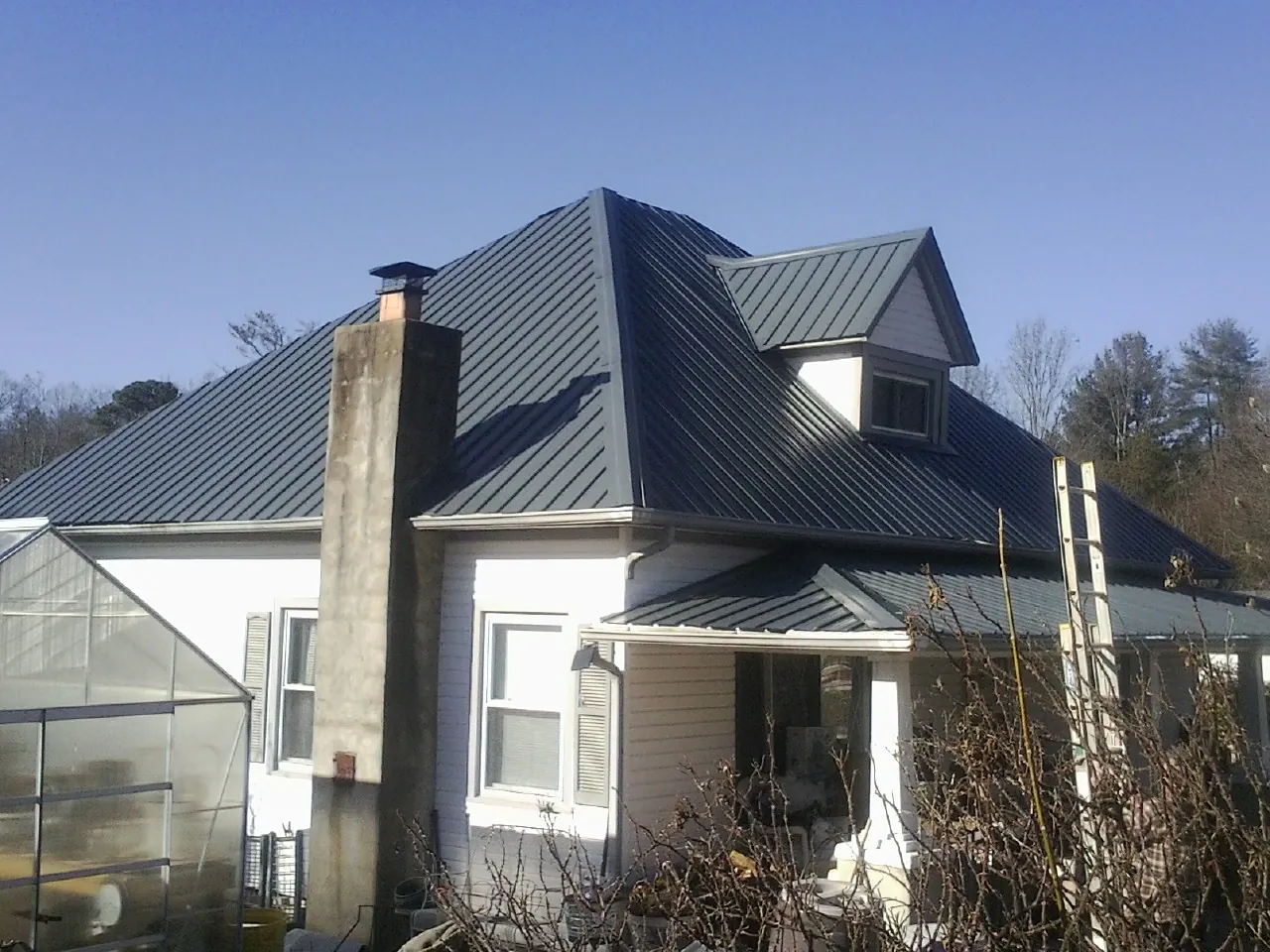 Dark blue standing seam metal roof on a white farmhouse with dormer — Slate & Tile Roof Repair by Roofing Brothers in Converse