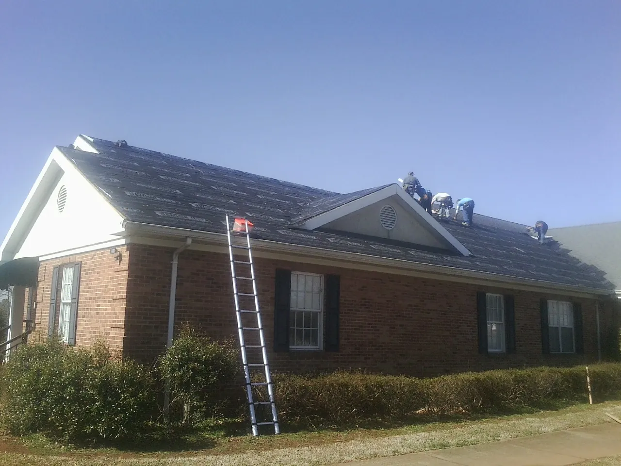 Crew tearing shingles off a brick ranch roof with a ladder set — Metal Roof Repair work by our crew in Converse