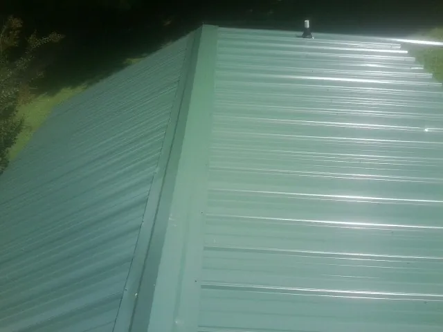 New green metal panels meeting at the ridge of a roof — Flat Roof Repair work by our crew in Converse