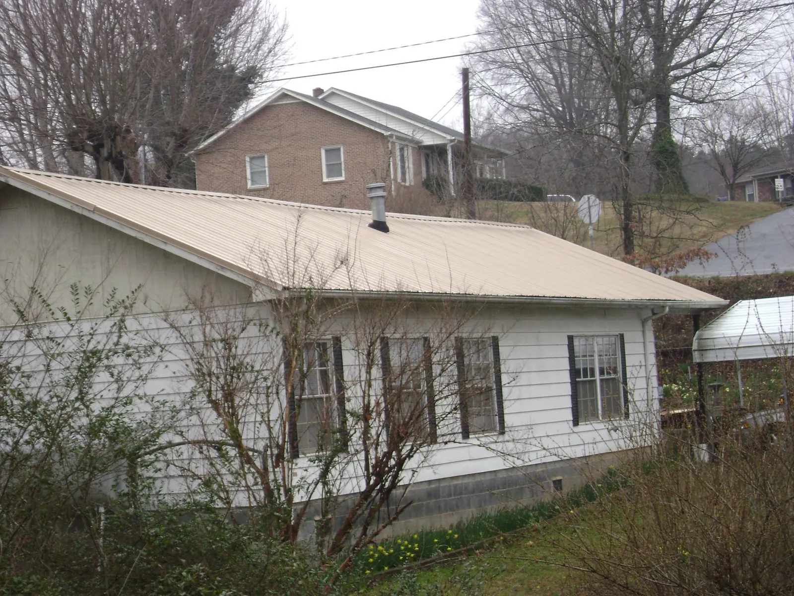 Tan metal roof on a white sided house set into a hillside — Commercial Roofing by Roofing Brothers in Converse
